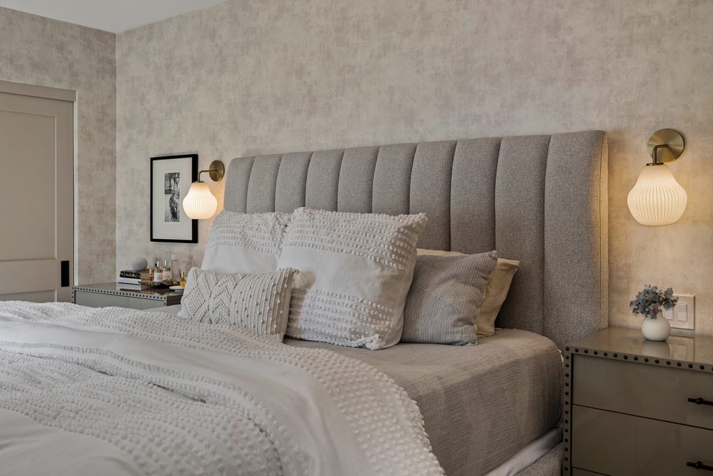 Channel tufted headboard framed by ribbed glass sconces and layered textured bedding