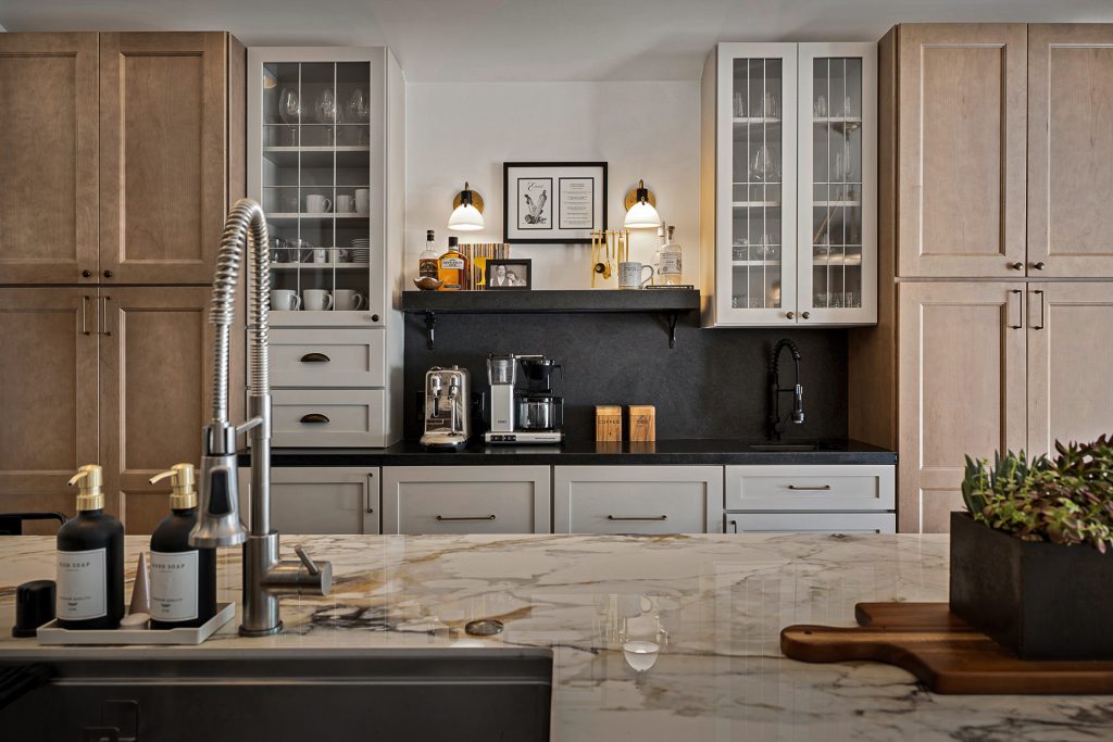 Coffee bar with a honed black stone counter and backsplash, glass front cabinets, and brass sconces