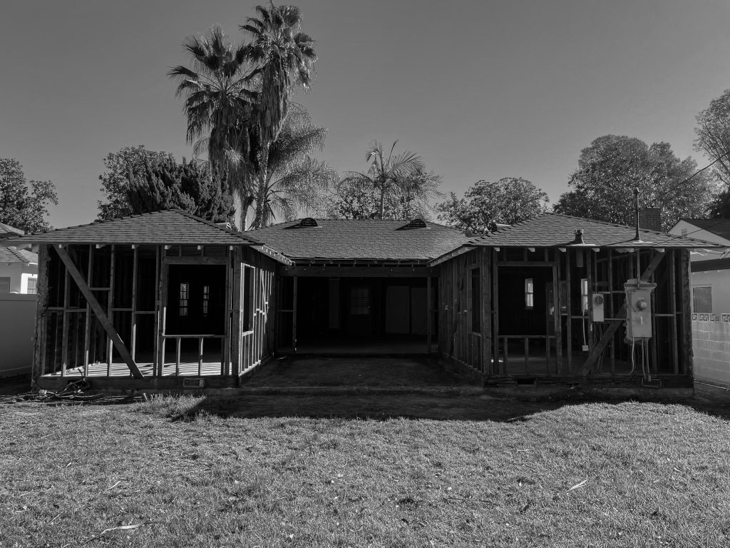 Rear of the house during construction, stripped back to its framing beneath the existing roofline