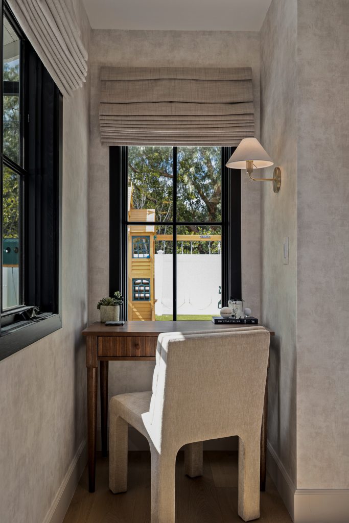 Desk nook in the primary bedroom with a walnut writing desk, brass sconce, and a linen roman shade