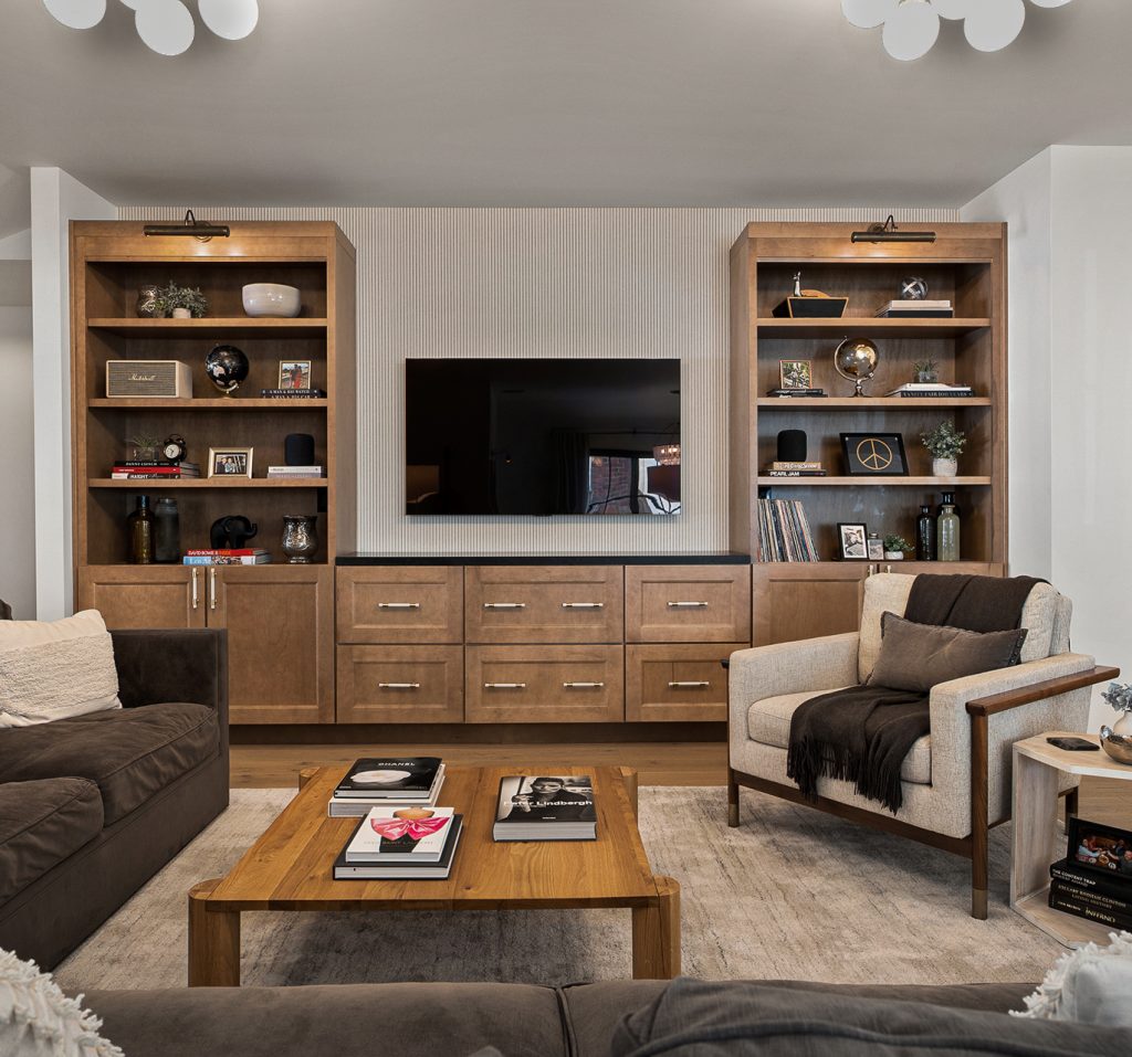 Finished living room with paired oak bookcases flanking a fluted panel wall and brass picture lights