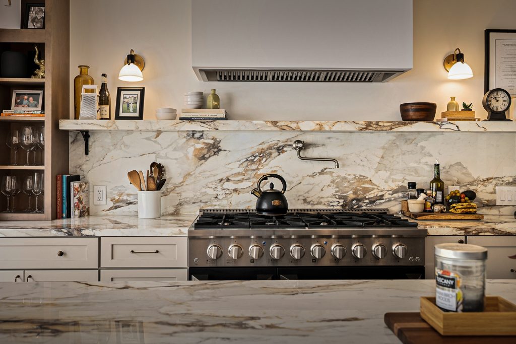 Range wall with a professional gas range set against a full height marble slab backsplash and a floating marble shelf