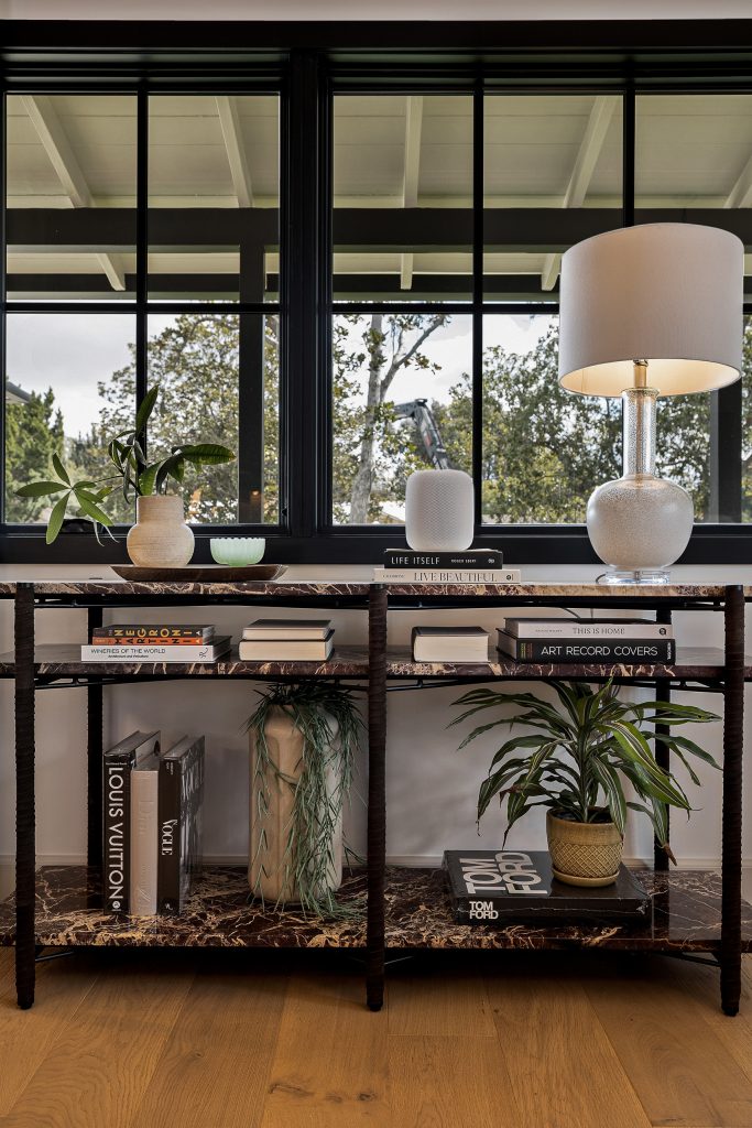 Marble and iron sideboard styled with books and lamplight beneath black framed windows