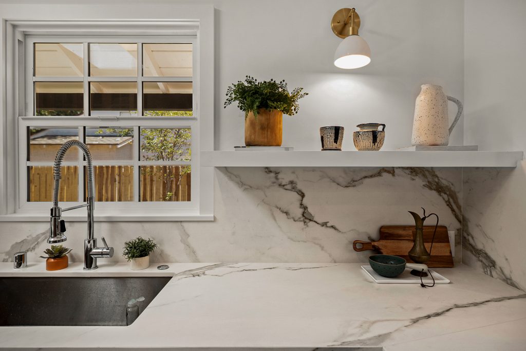 Kitchen sink detail with veined stone backsplash, open wood shelving, and brass fixtures