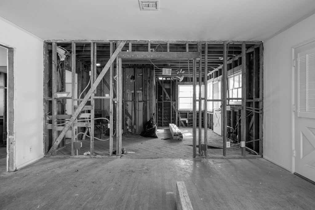 Black and white construction photo of the house stripped to wood framing during renovation