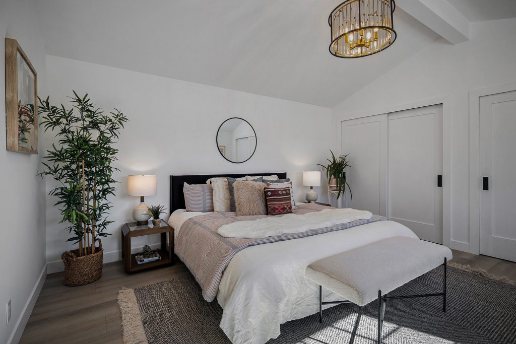 Primary bedroom under a vaulted ceiling with a black upholstered bed and a brass and glass chandelier