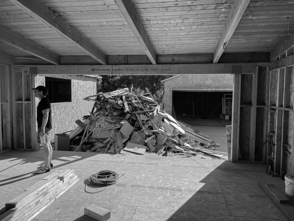 Dan Currier standing in the framed interior during construction, beside a pile of demolition debris