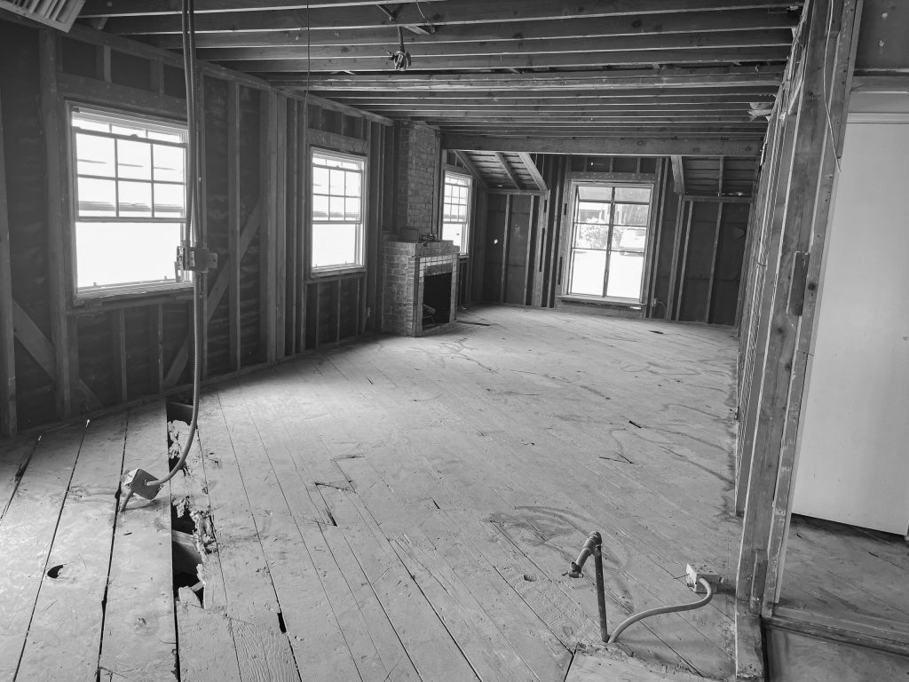 Living room during construction, stripped back to bare studs and ceiling joists around the original brick fireplace