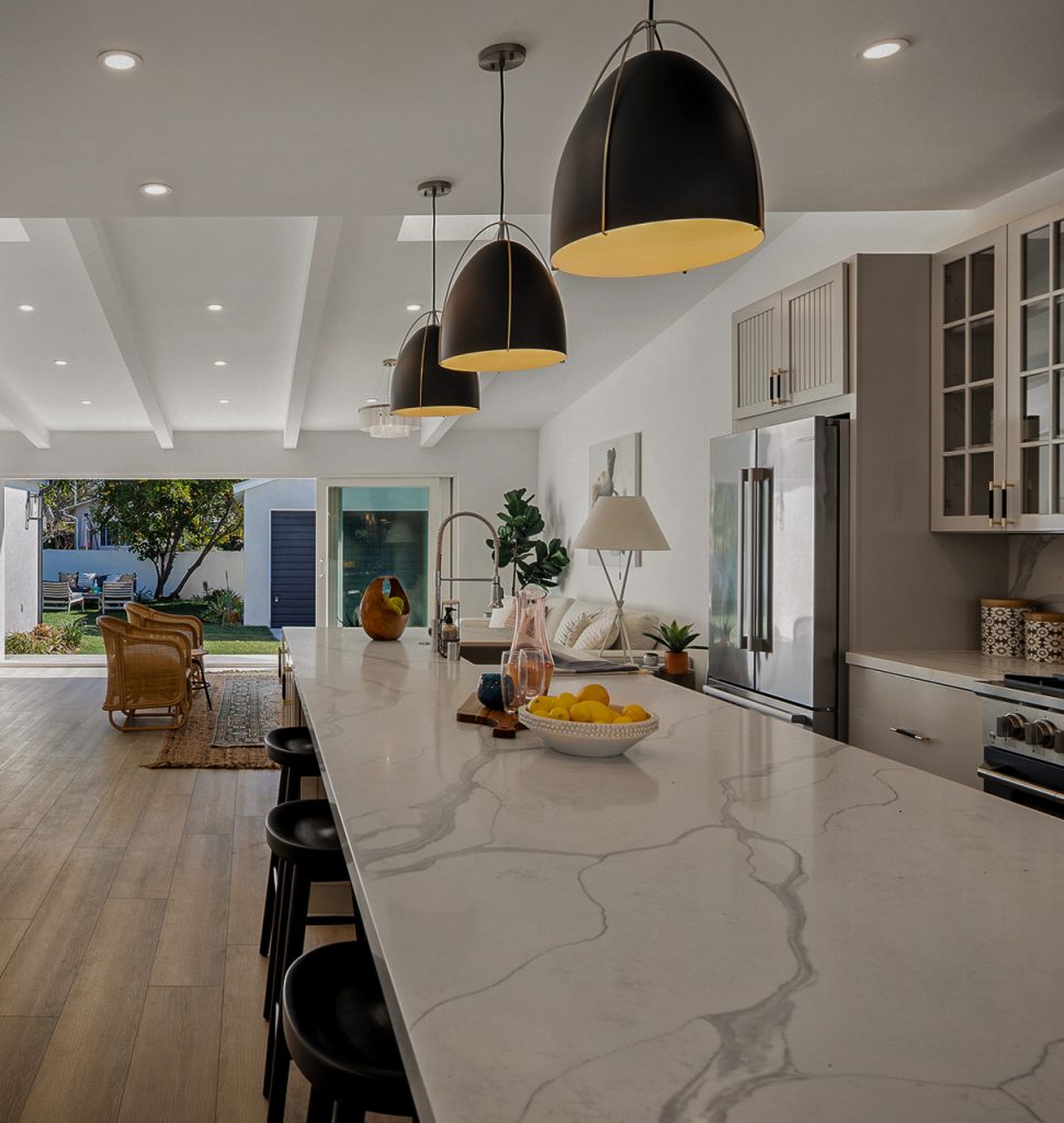 Marble island running the length of the kitchen toward sliding glass doors opened to the backyard, lit by three black dome pendants