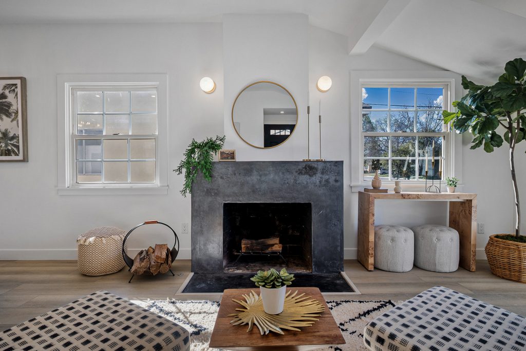 Finished living room with a blackened steel fireplace surround, round mirror, and paired globe sconces