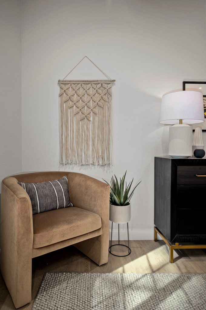 Camel velvet barrel chair beneath a macrame wall hanging, with a black nightstand alongside
