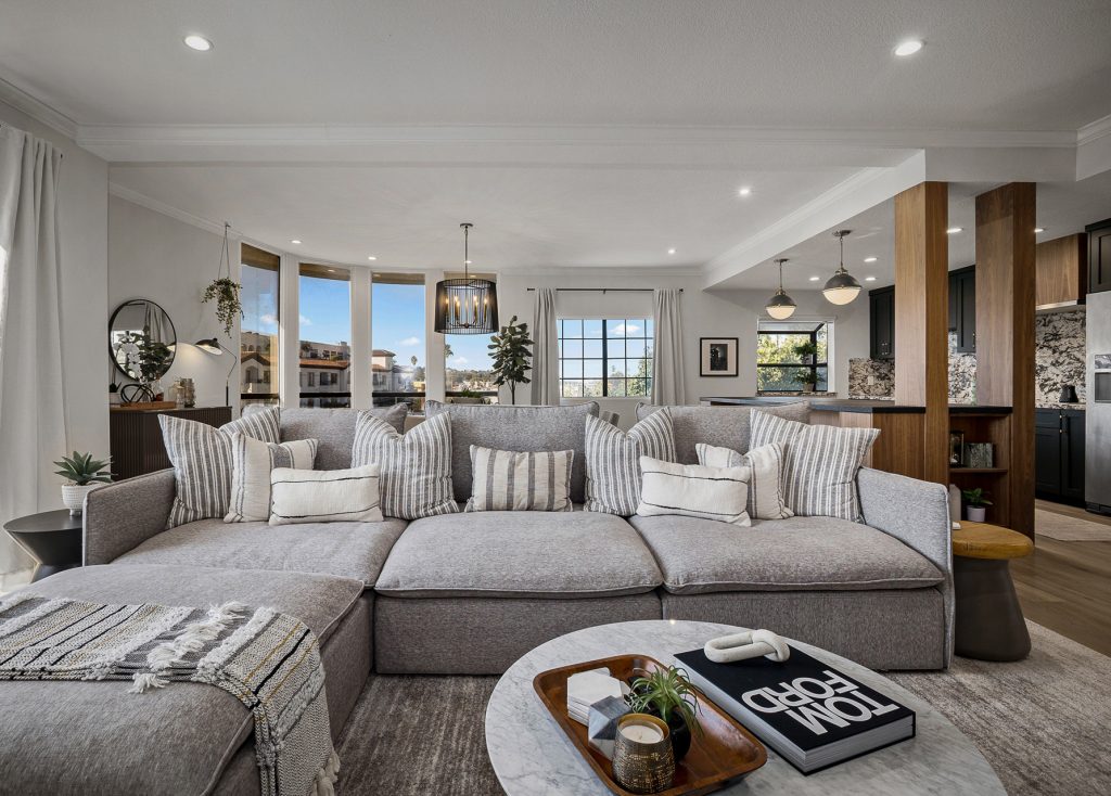 Living room with a deep grey sectional, marble coffee table, and a walnut column framing the kitchen beyond