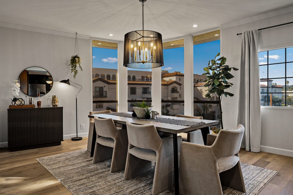 Dining room with a black cage chandelier, velvet chairs, and corner windows over the neighboring rooftops