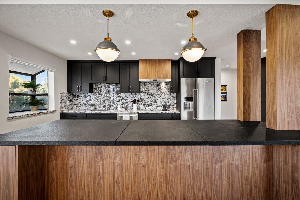 Kitchen island in walnut with a black stone top, set under dome pendants against dark cabinetry