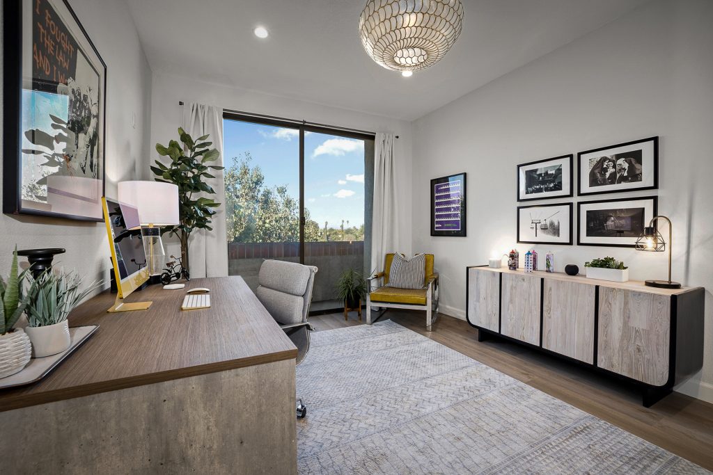 Home office with a wide desk, a gallery wall of black and white photographs, and a capiz shell pendant