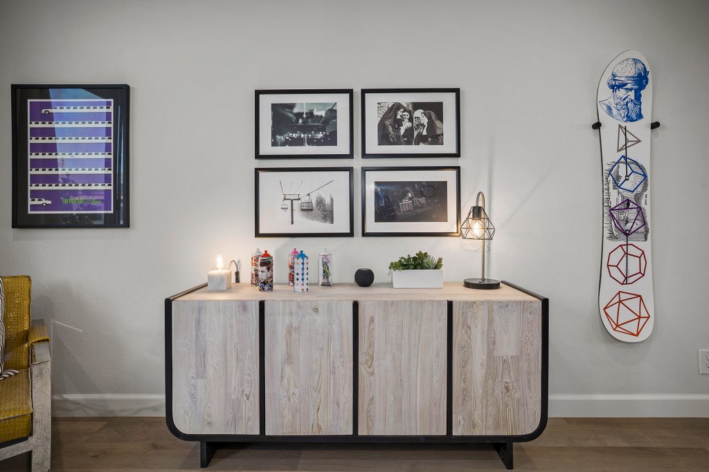 Office wall with a graphic snowboard mounted beside a bleached wood credenza and a gallery of black and white photographs