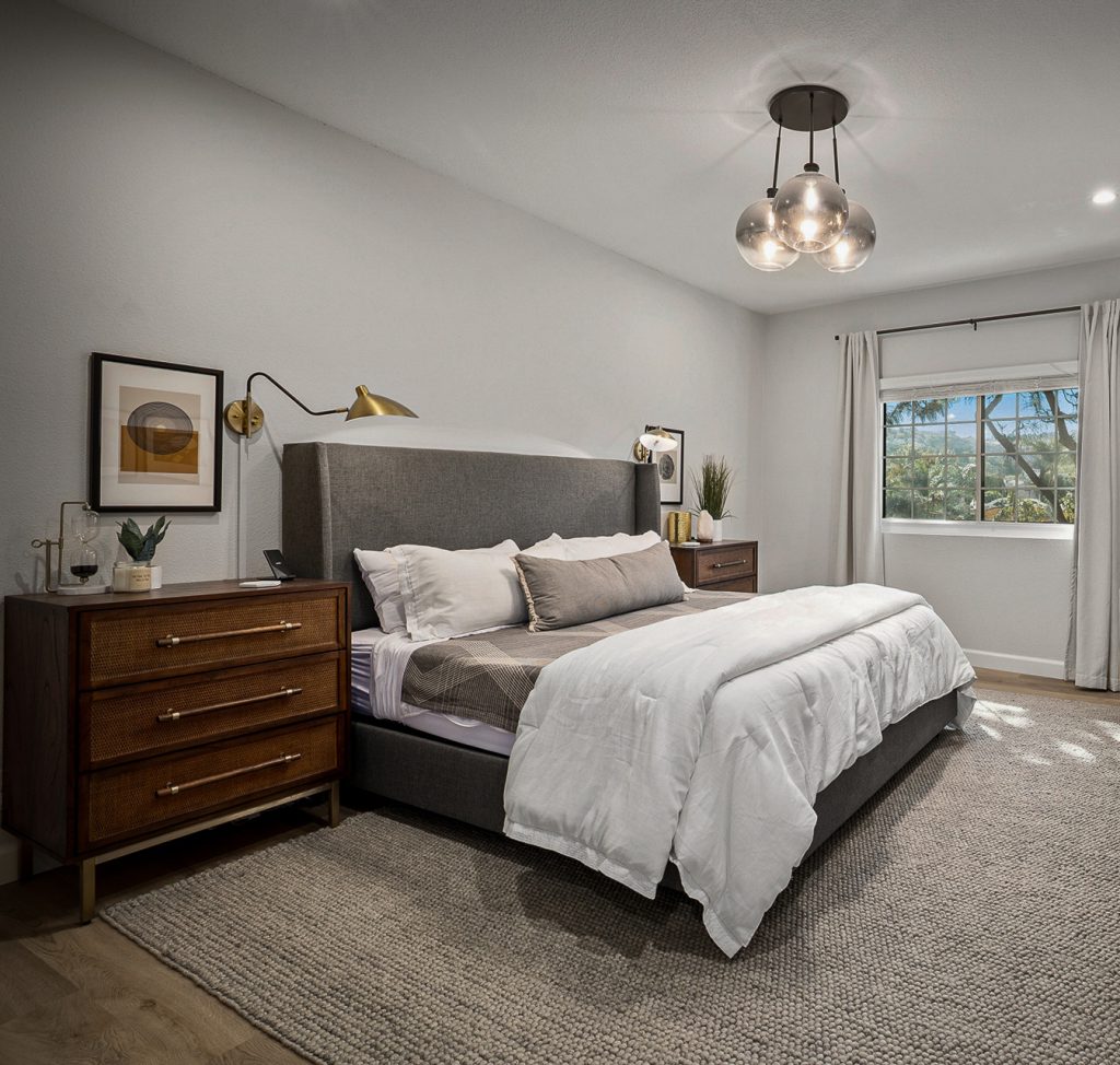 Primary bedroom with a grey wingback bed, cane fronted nightstands, and a smoked glass cluster pendant
