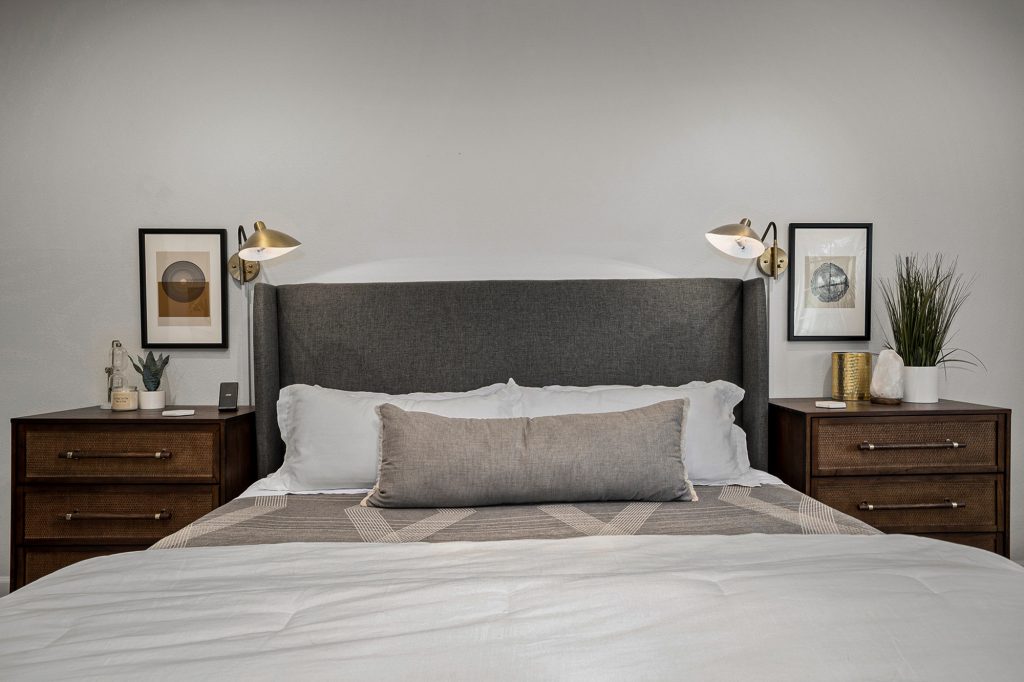 Primary bed framed symmetrically by brass sconces and matching cane fronted nightstands