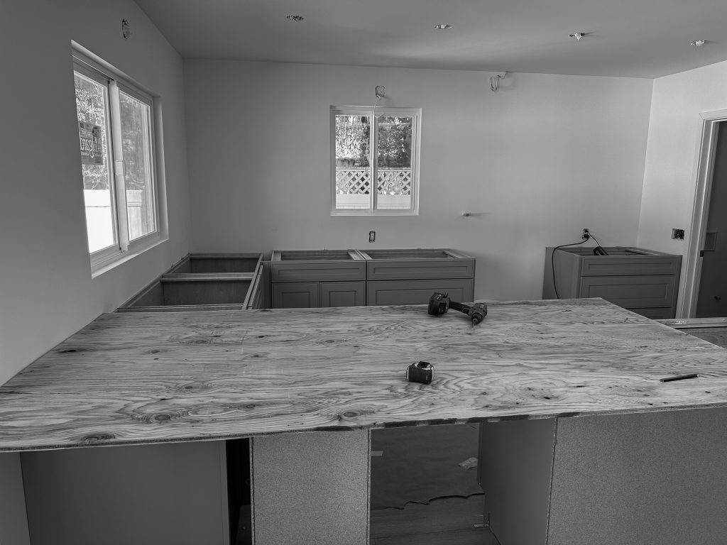 Kitchen during construction with the new cabinet boxes set and a plywood template on the island awaiting stone