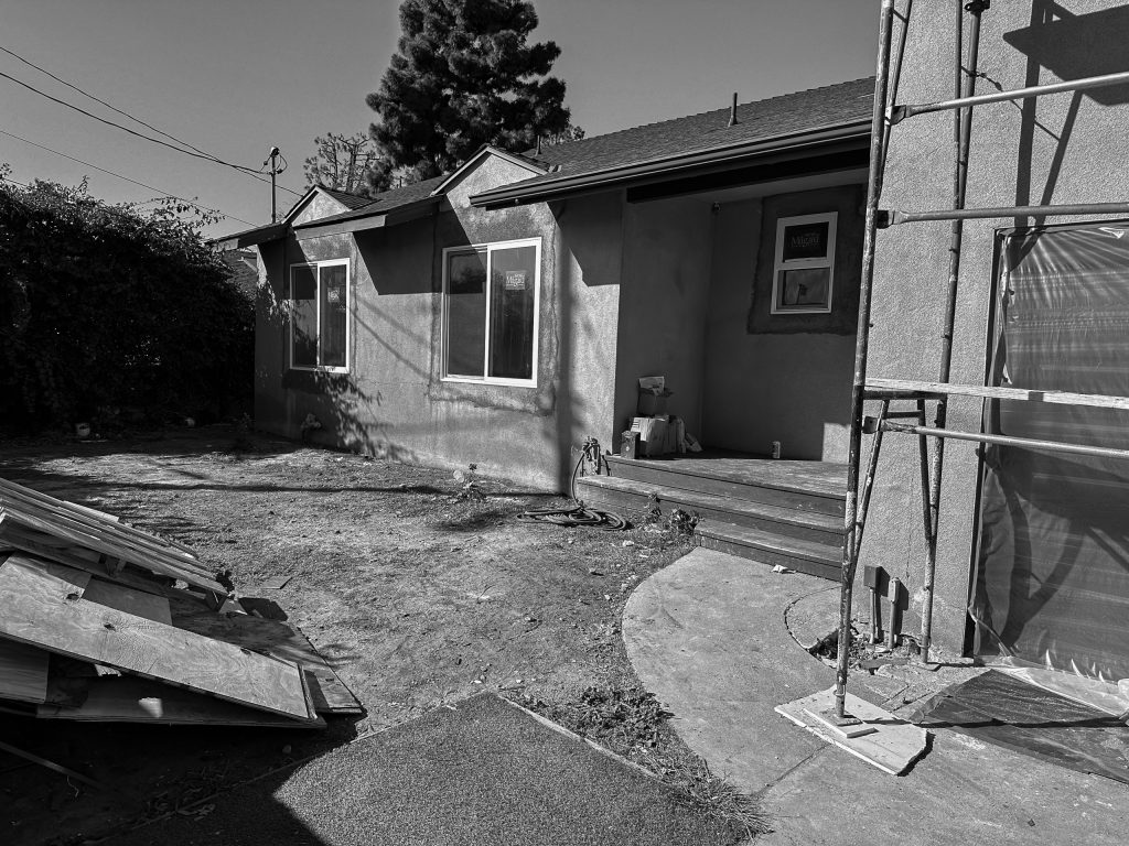 Rear of the house during construction, with scaffolding and stacked lumber against the original stucco