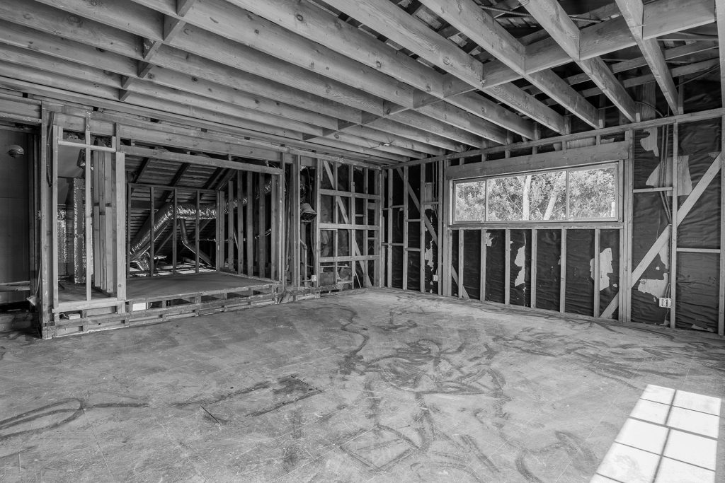 Primary bedroom during construction, framed back to the studs with a new window opening and exposed ceiling joists