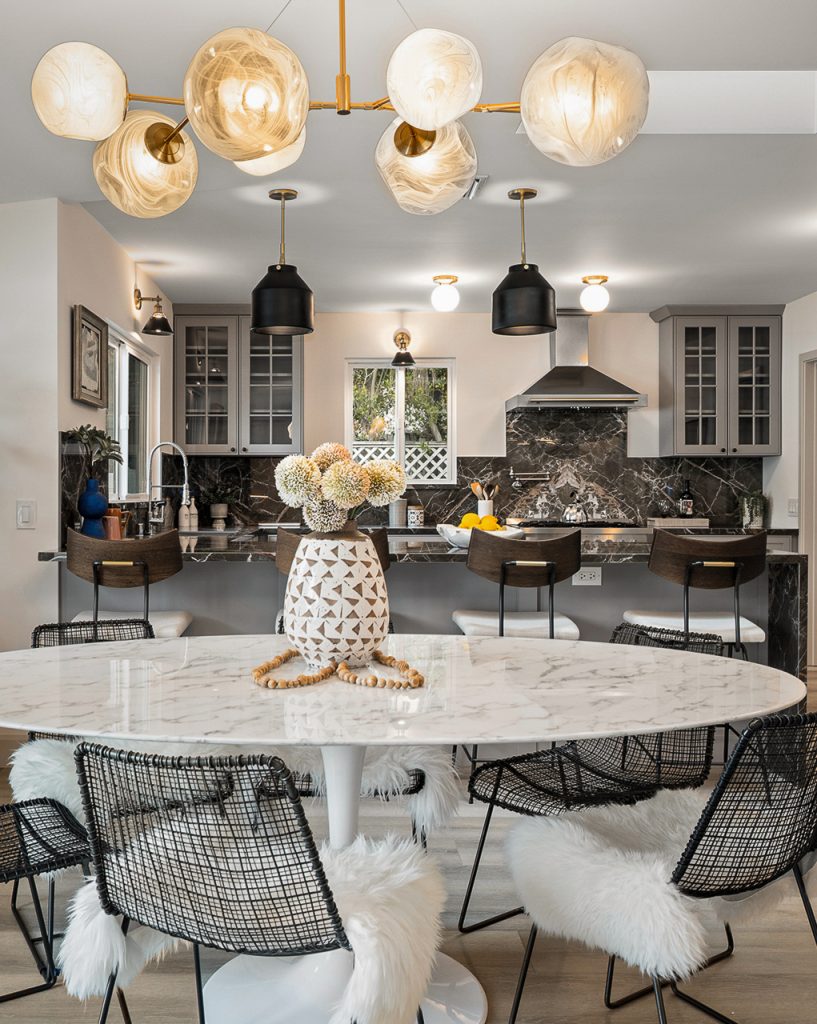 Dining area with a round marble table, black wire chairs, and a marbled glass globe chandelier open to the kitchen