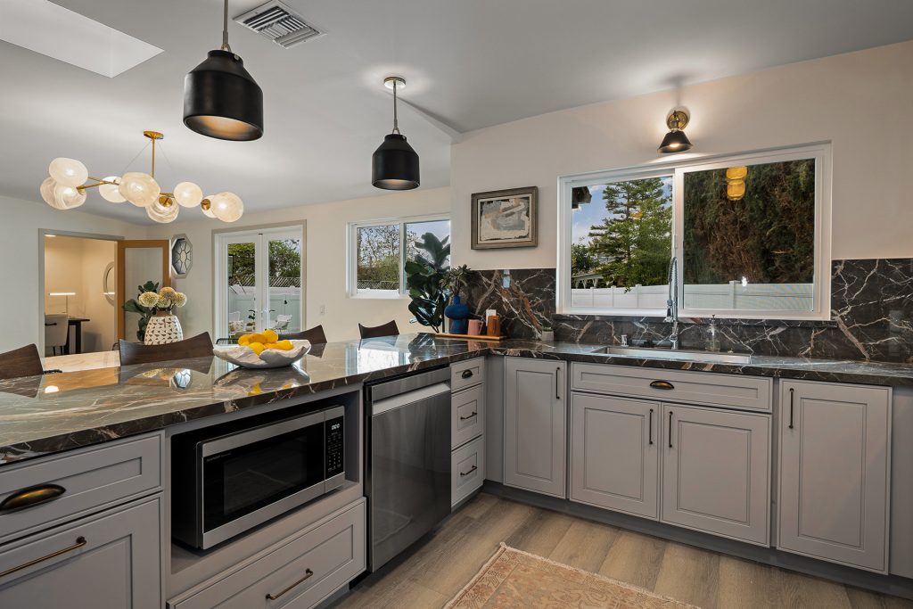Kitchen from the sink side, with dark marble counters running beneath a brass sconce and the dining room beyond