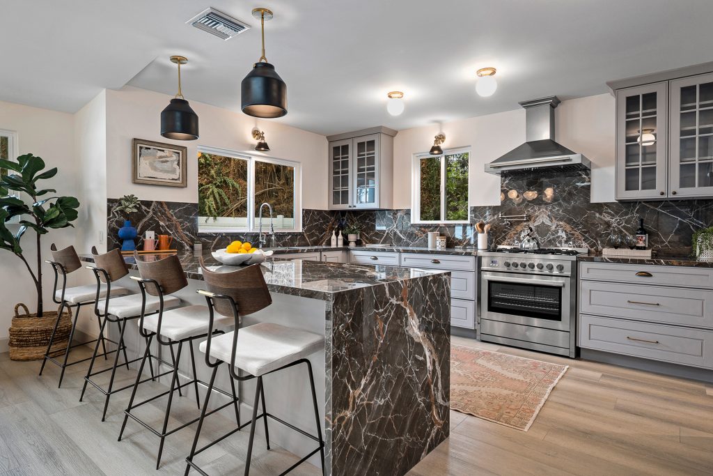 Kitchen with a dark veined marble waterfall island, grey cabinetry, and black dome pendants