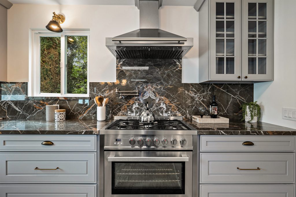 Range wall with a stainless range and hood set against a dark marble slab backsplash with copper veining