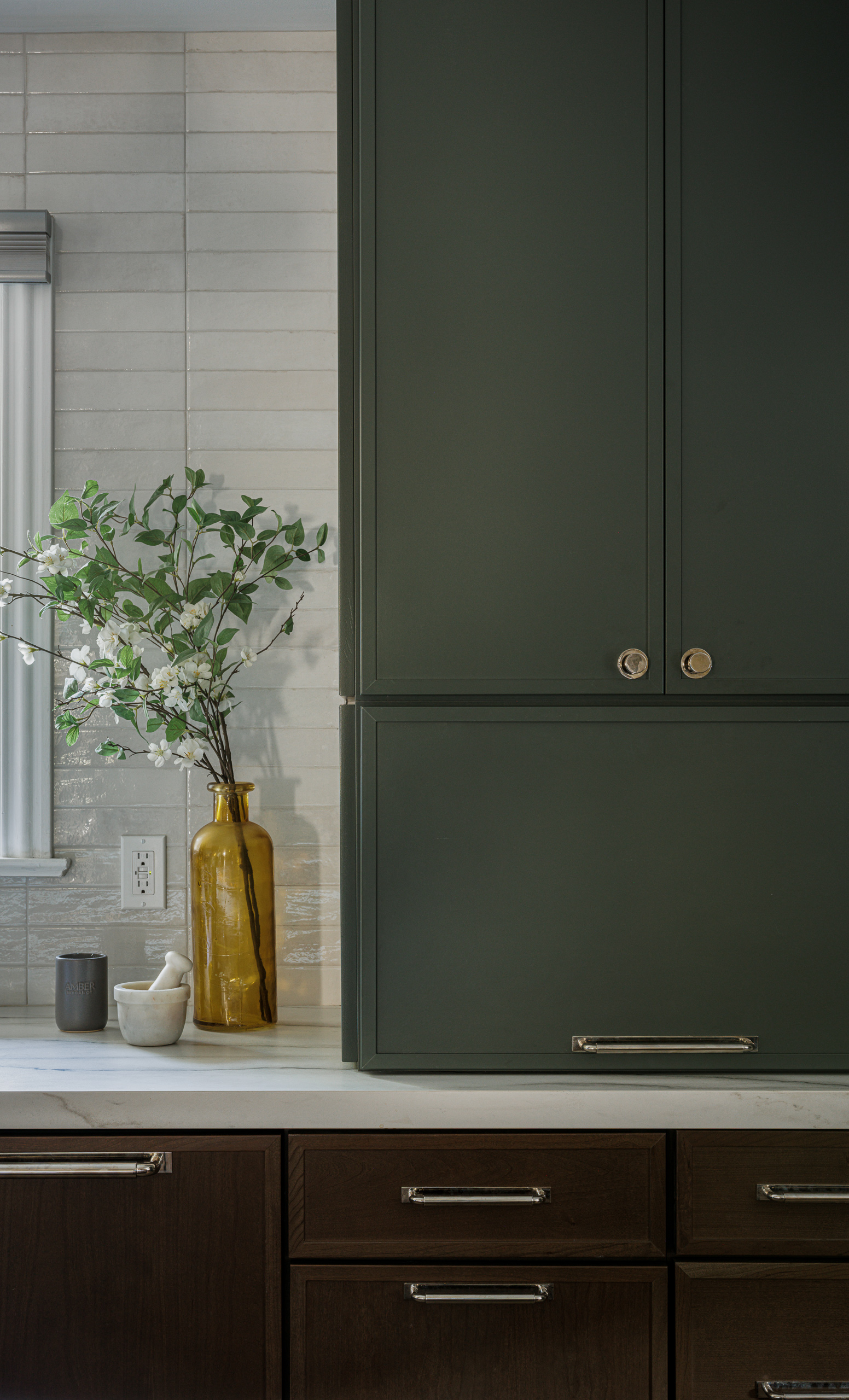 A tall deep green cabinet with a lift-up appliance garage door, beside glazed white tile and a marble counter.