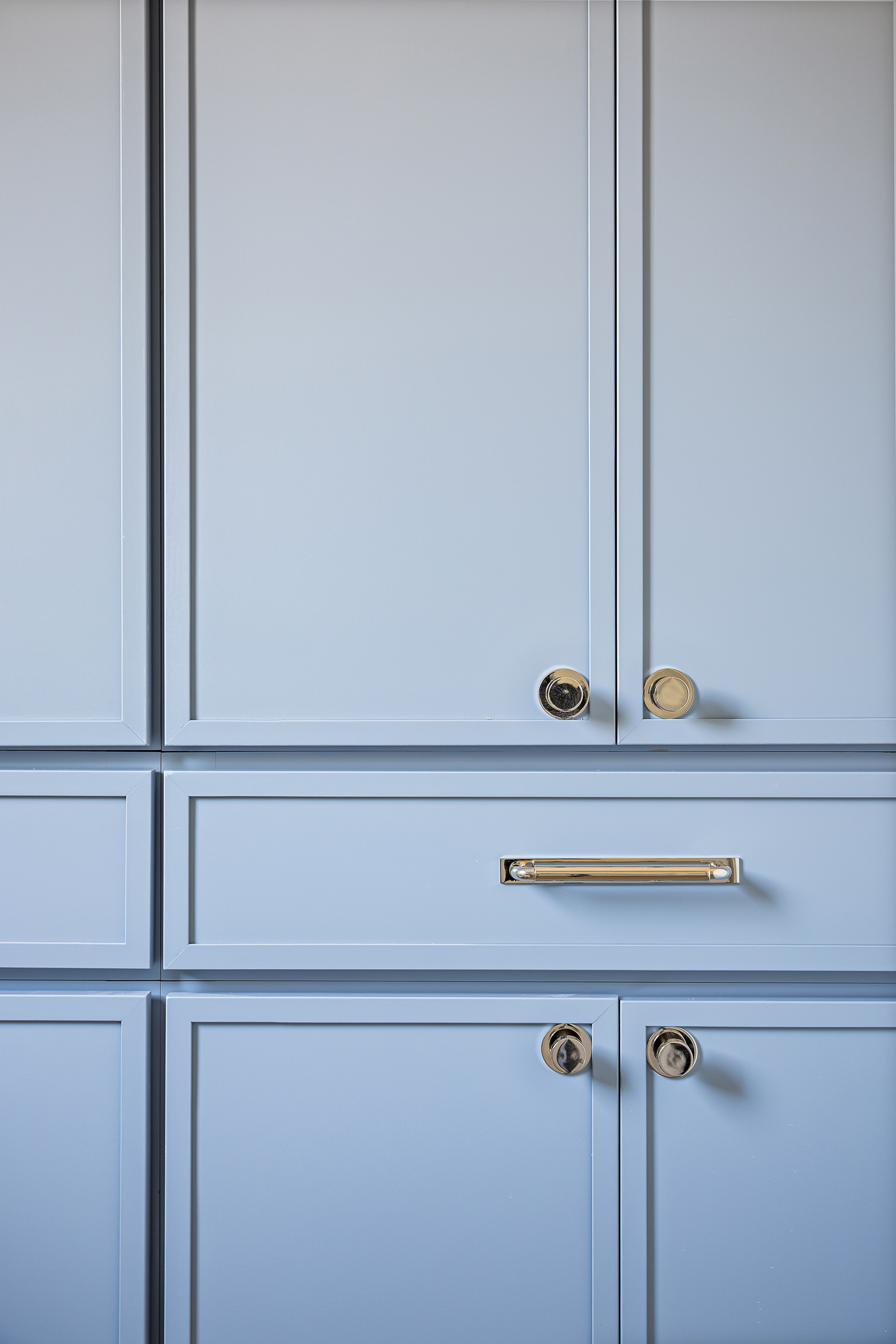 Soft blue cabinetry with polished brass knobs and a recessed brass drawer pull.