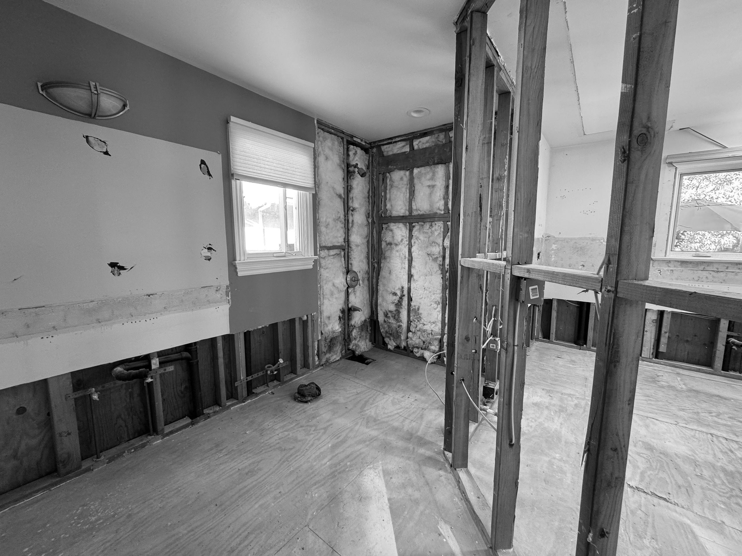 The bathroom during construction after the tub and shower were removed, open framing and insulation where the enclosure had been.