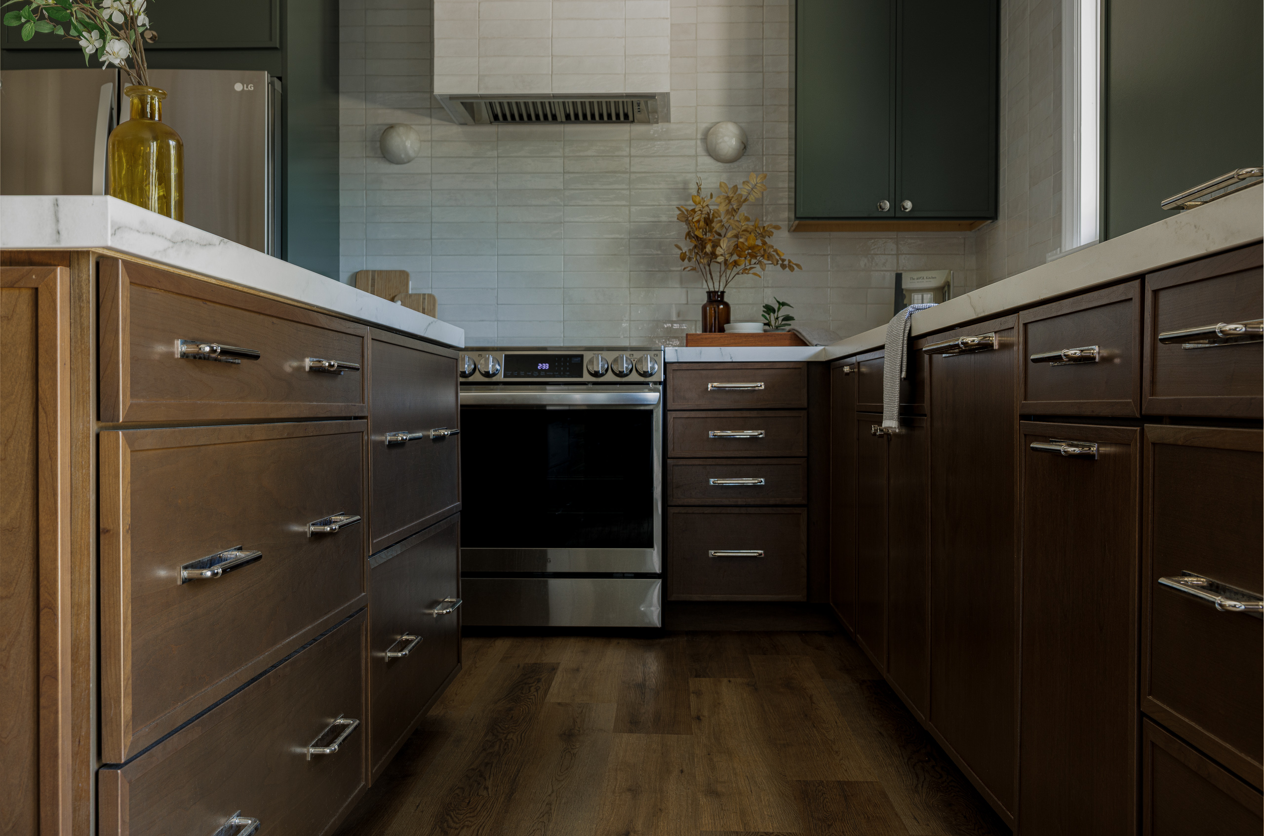 A run of dark wood lower cabinets and drawers with polished nickel hardware leading to the range, over wide plank oak flooring.