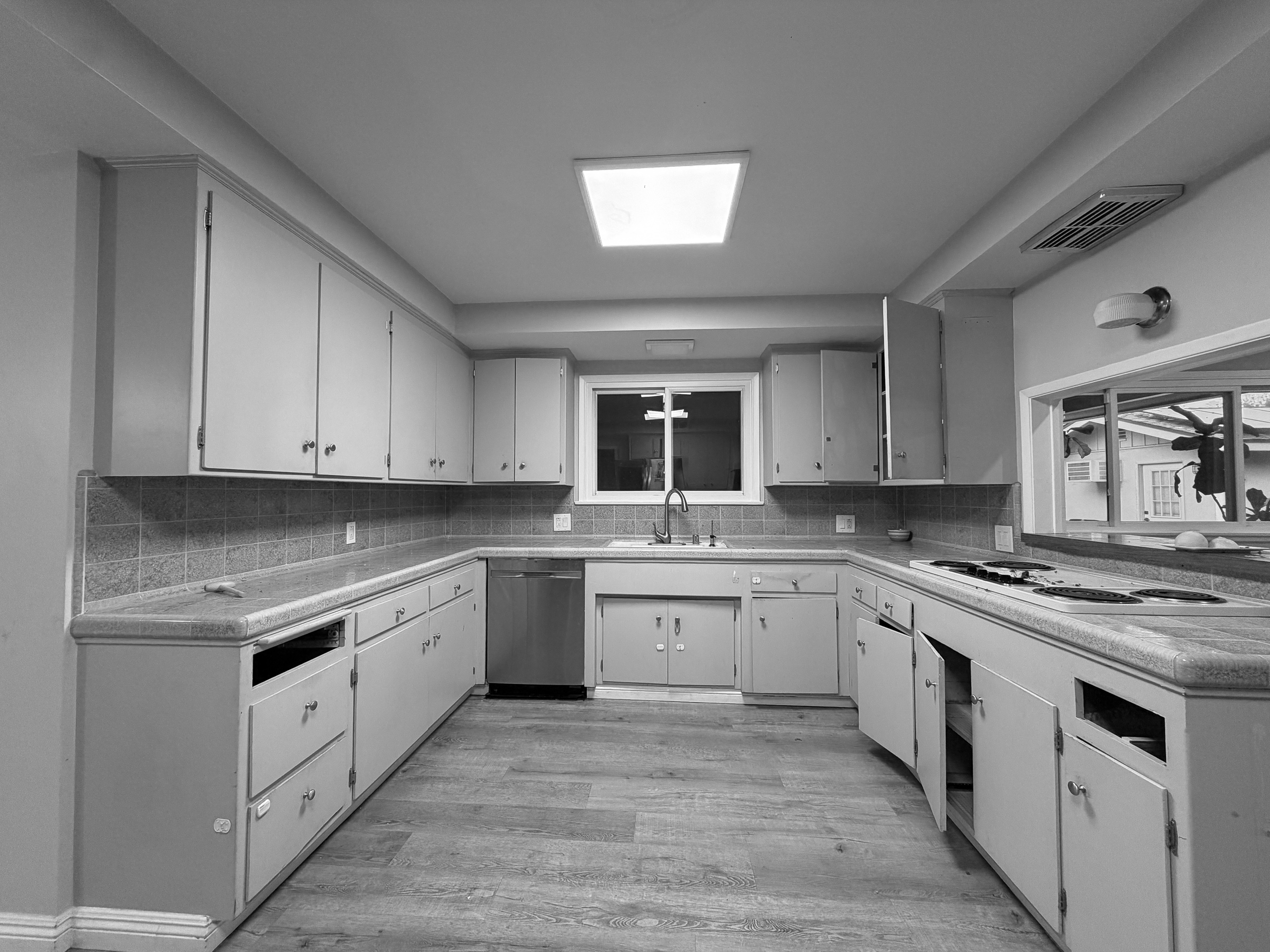 The original 1960s kitchen before renovation, a closed U shaped layout with flat panel cabinets, tile counters and a fluorescent ceiling panel