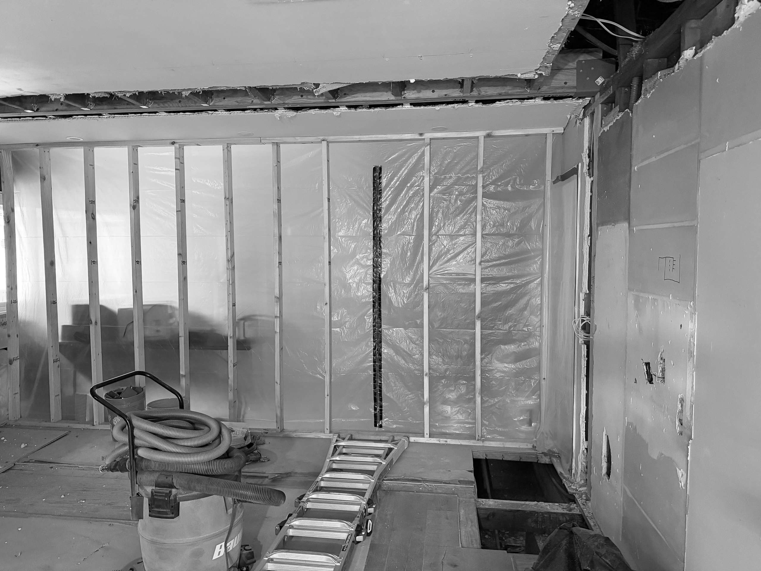 During construction, a stud wall sealed in plastic sheeting with the ceiling opened up and a shop vacuum and ladder on the protected floor