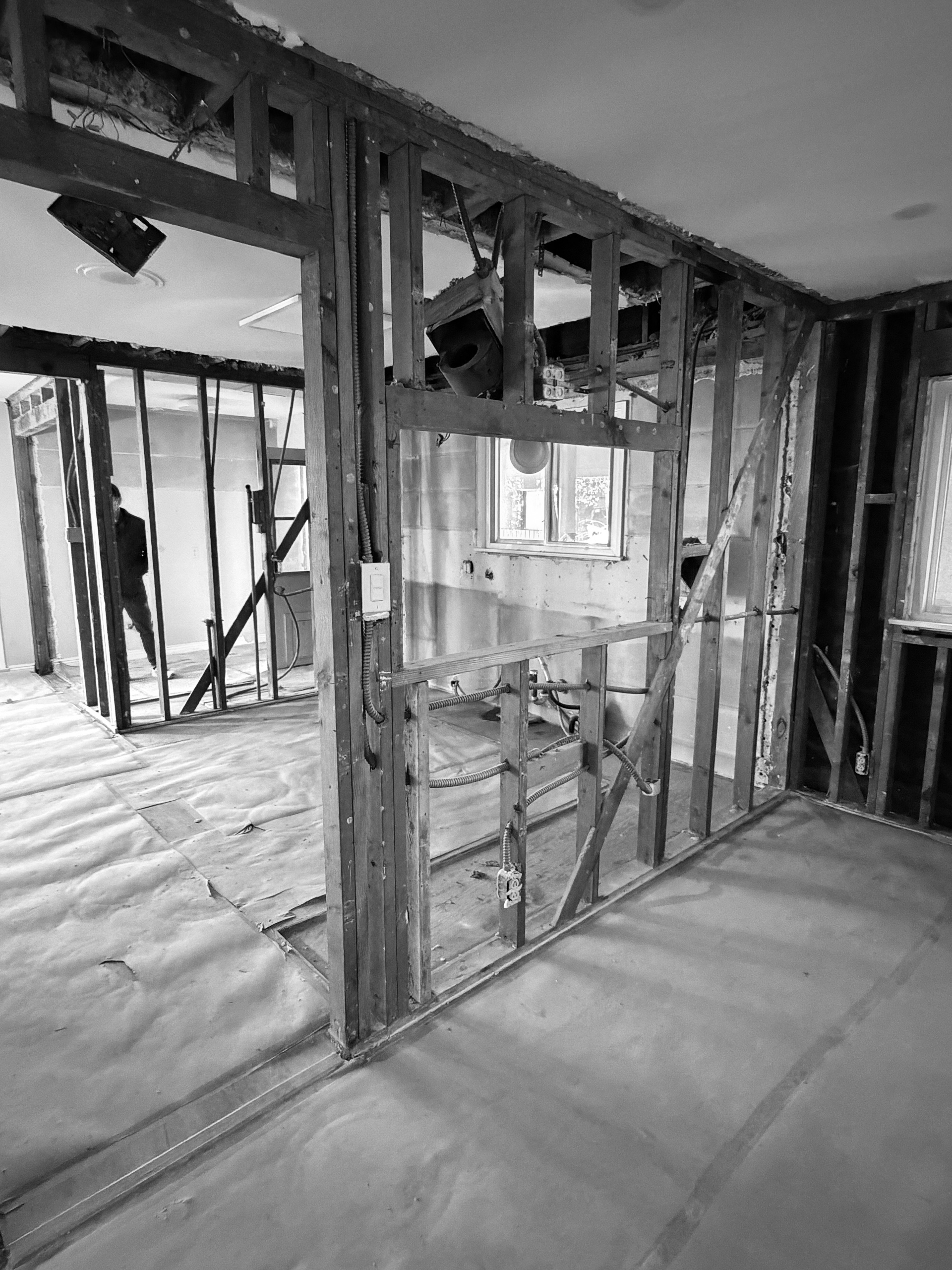 Open framing during construction with the wall between the kitchen and dining room removed, exposing studs, wiring and the rooms beyond