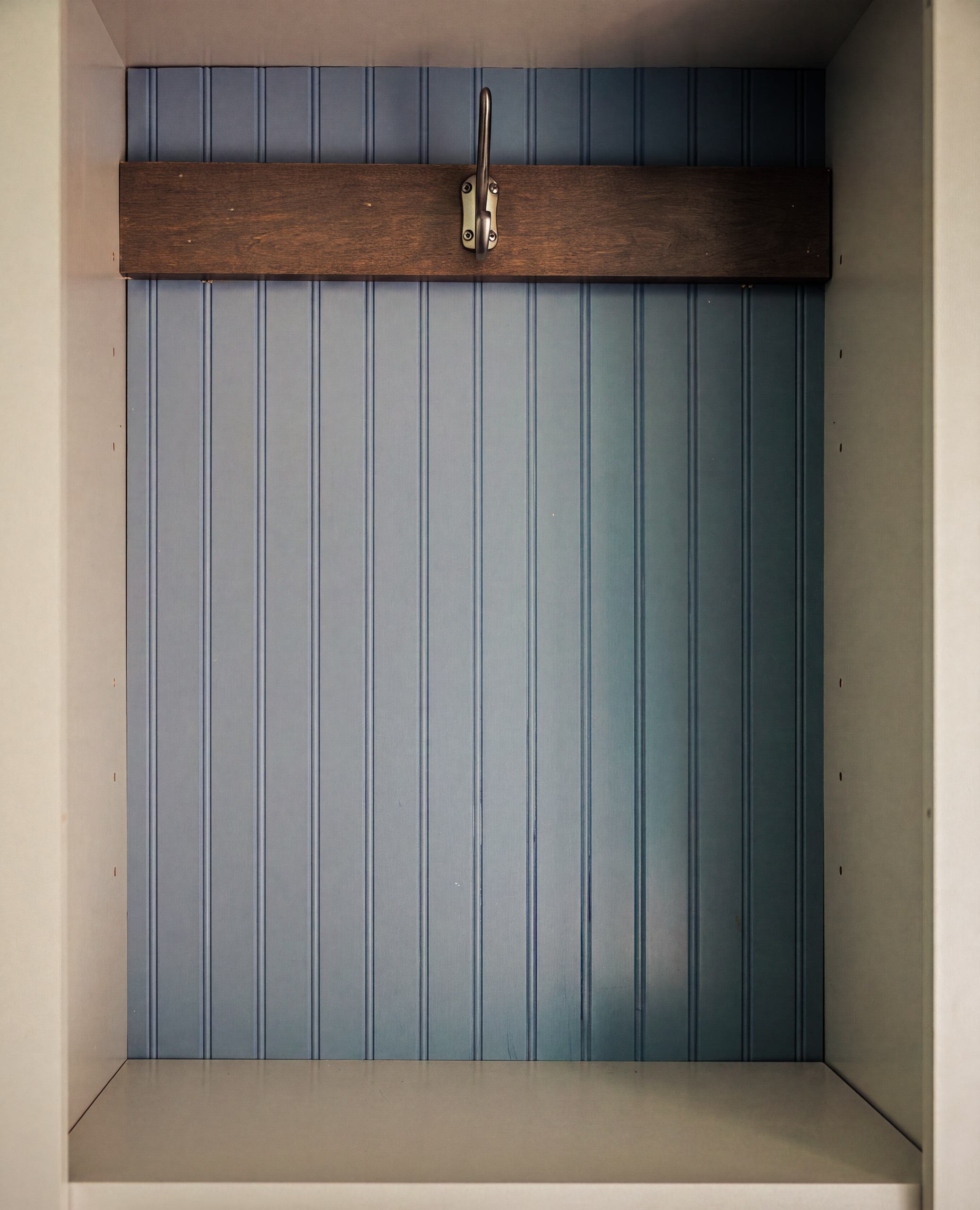 Mudroom cubby lined in blue beadboard with a brass hook mounted on a dark wood rail above the bench