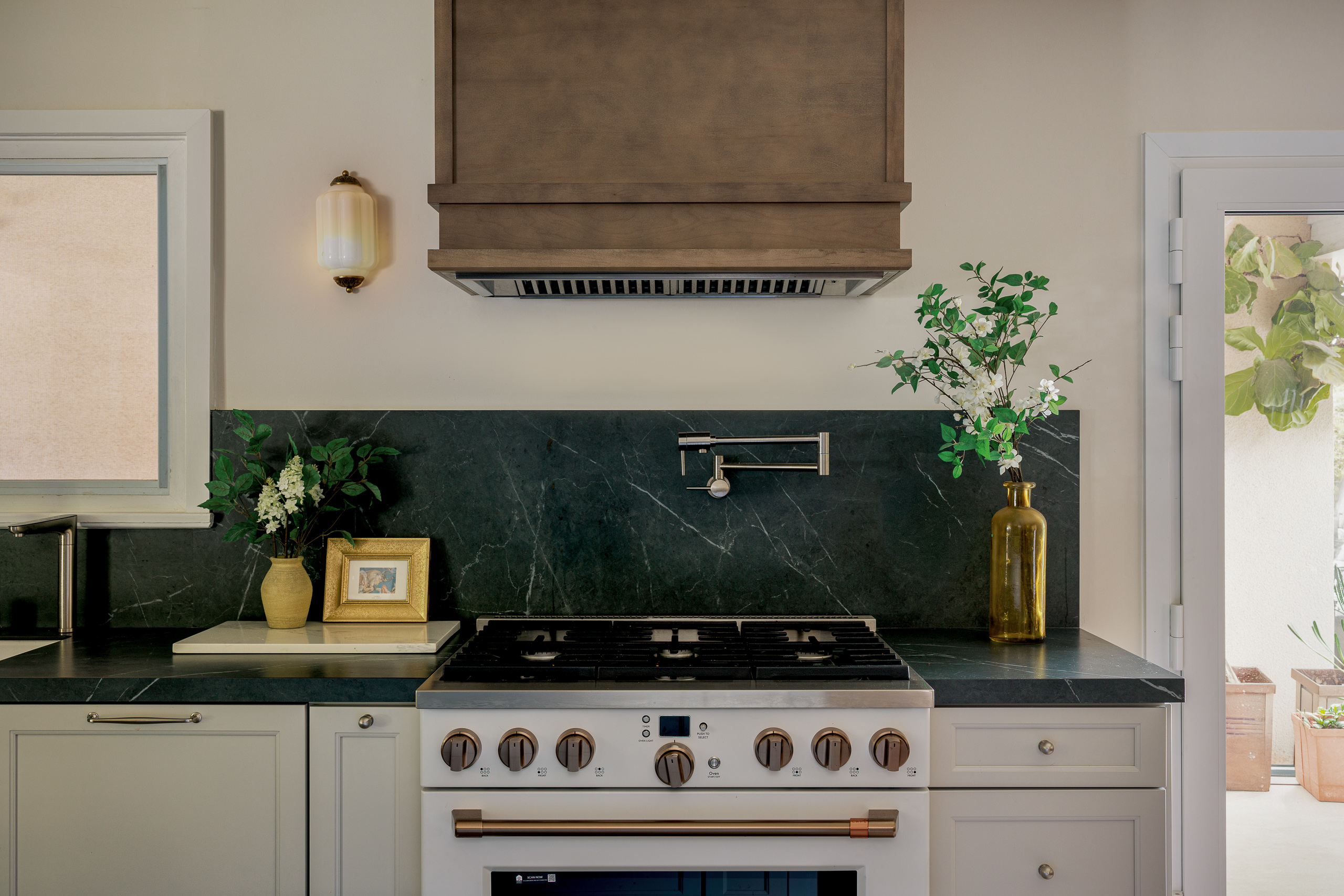 White range with copper hardware under a custom stained wood hood, framed by soapstone counters and a doorway to the garden
