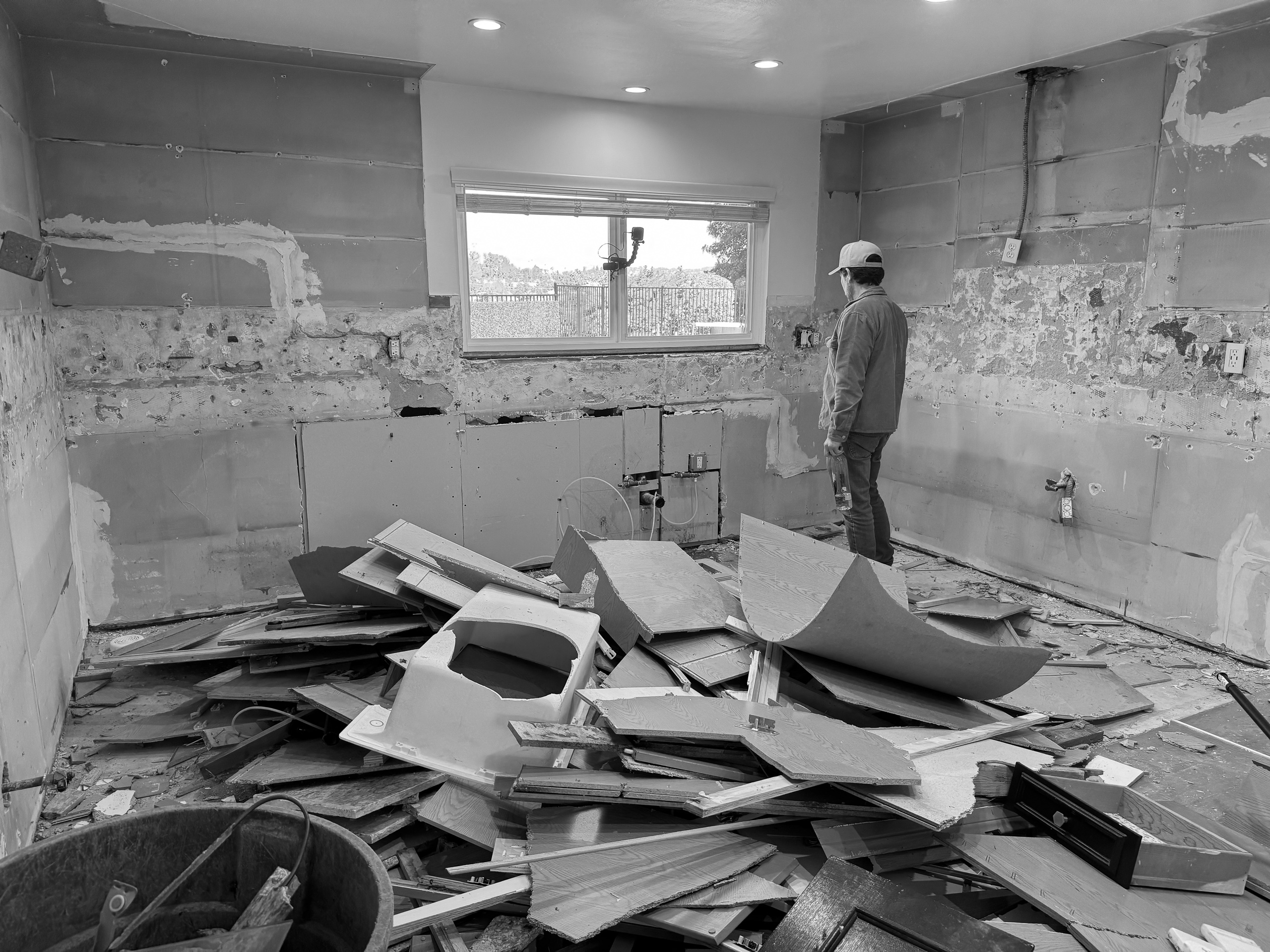 The room stripped to bare walls during construction, with a crew member standing beside a pile of removed cabinetry and flooring